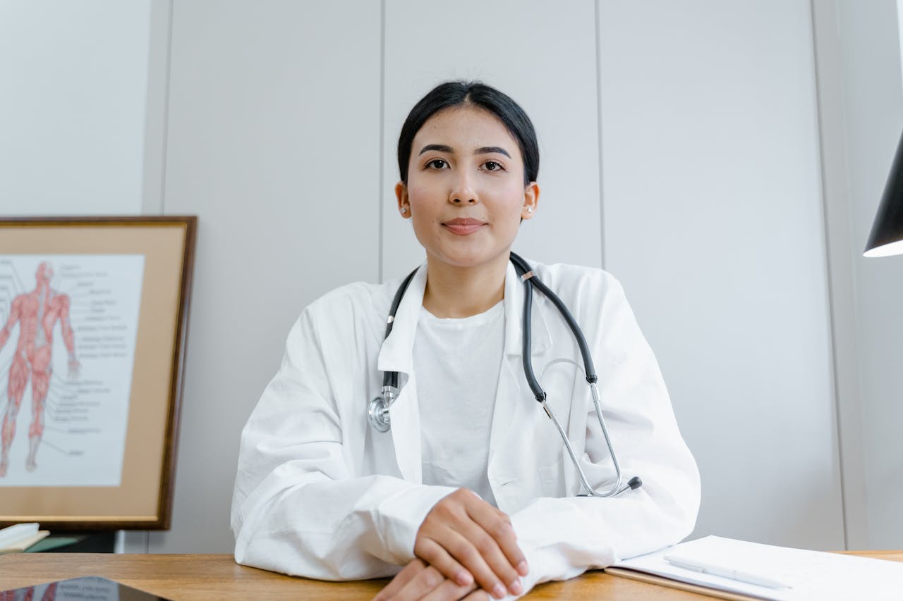 creative-02 A female doctor confidently sits at her desk, ready for consultation in a medical office.